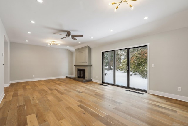 unfurnished living room with lofted ceiling, a large fireplace, ceiling fan with notable chandelier, and light hardwood / wood-style floors