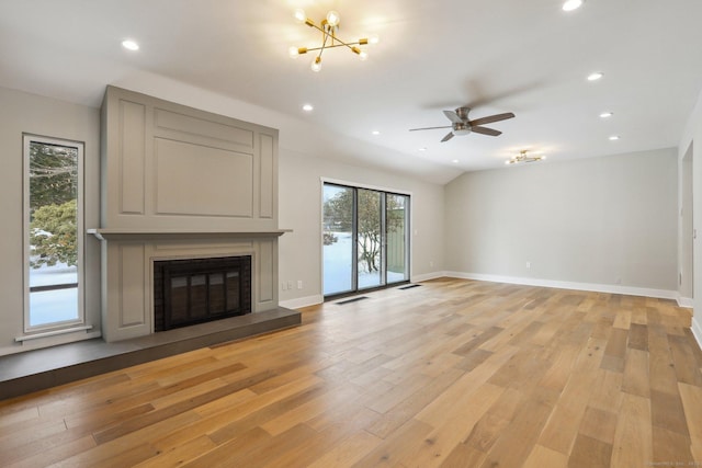 unfurnished living room featuring lofted ceiling, ceiling fan with notable chandelier, and light hardwood / wood-style flooring