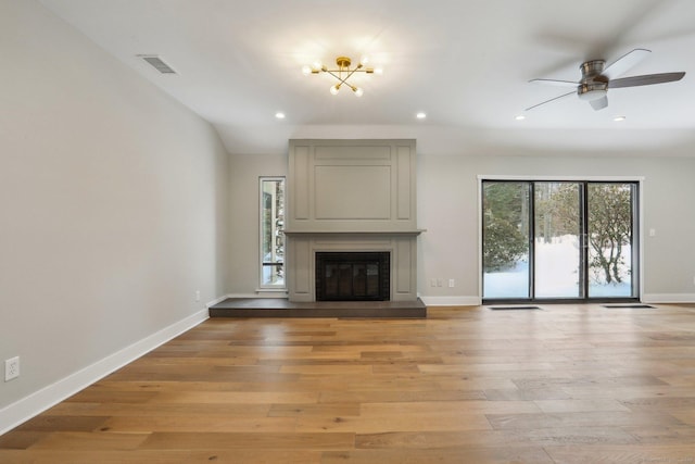 unfurnished living room with ceiling fan, a large fireplace, and light wood-type flooring