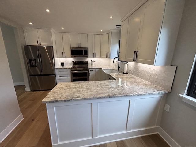 kitchen featuring wood finished floors, baseboards, a peninsula, tasteful backsplash, and appliances with stainless steel finishes