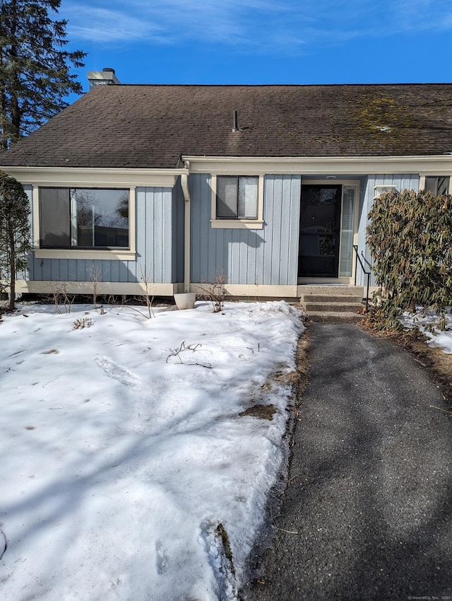 snow covered property entrance featuring roof with shingles and board and batten siding