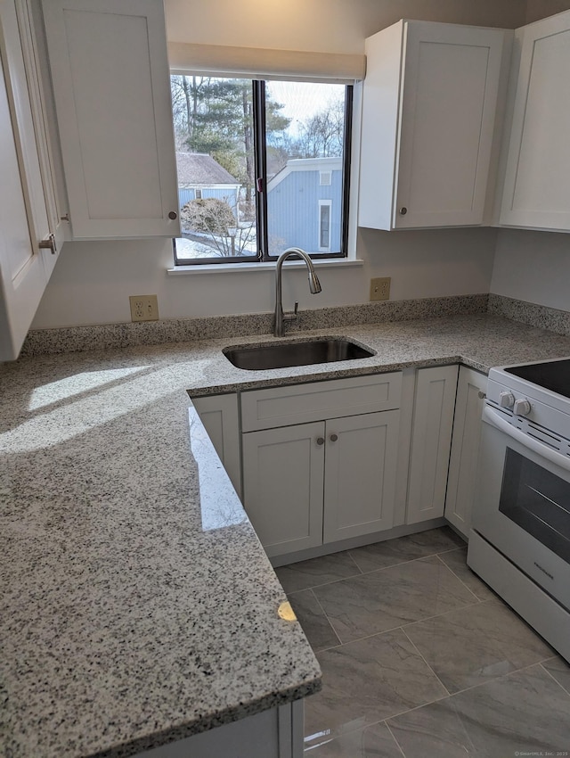 kitchen featuring light stone countertops, white electric range, white cabinets, and a sink