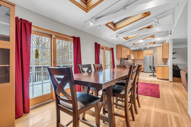 dining space with rail lighting, vaulted ceiling with skylight, and light hardwood / wood-style flooring