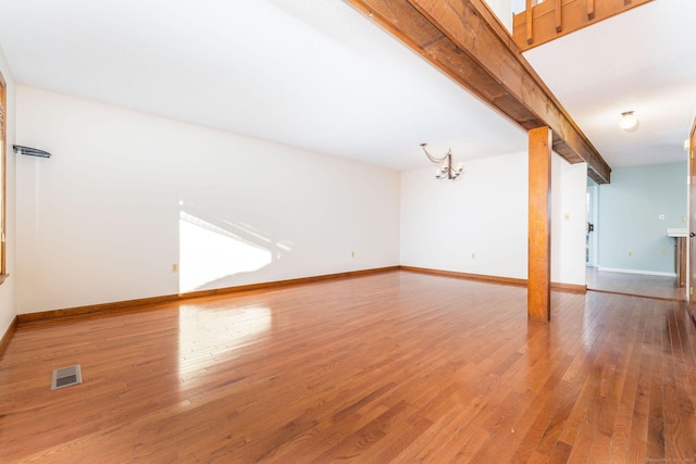 unfurnished living room with an inviting chandelier, wood-type flooring, and beamed ceiling