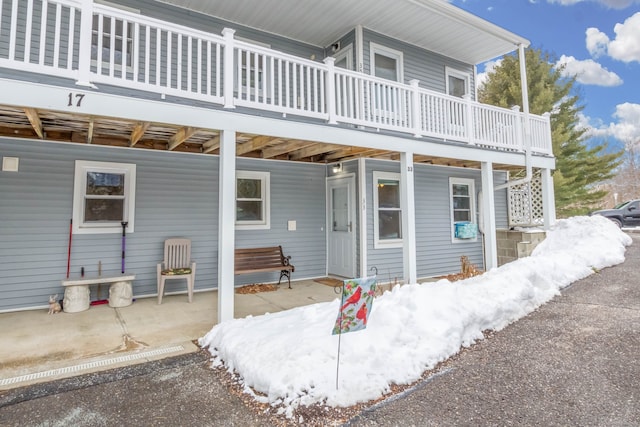 snow covered back of property with a wooden deck and a patio