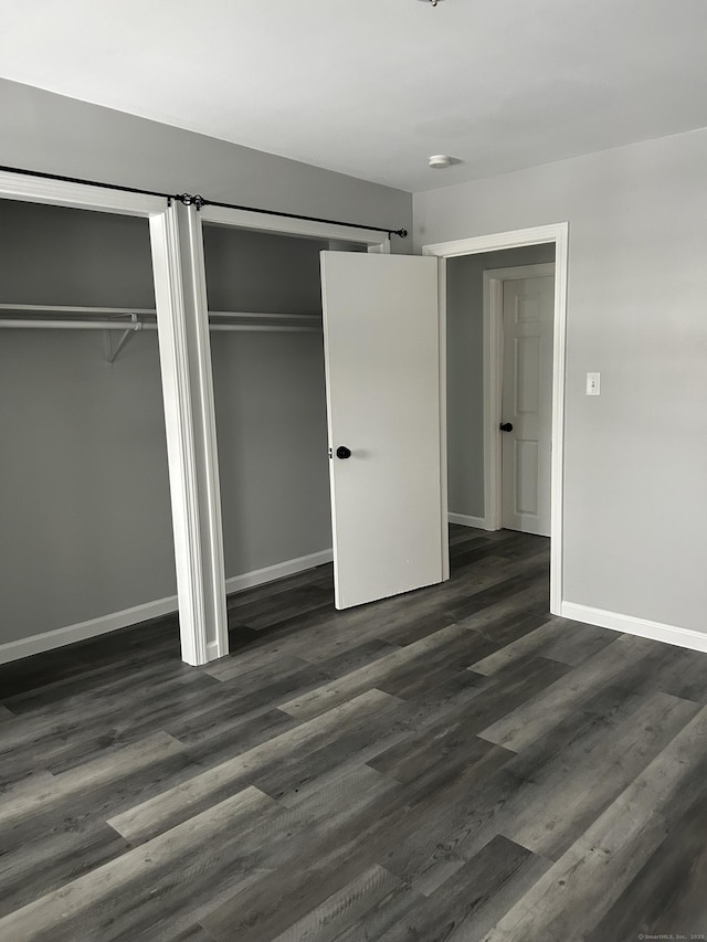 unfurnished bedroom with baseboards, a barn door, dark wood-style flooring, and multiple closets