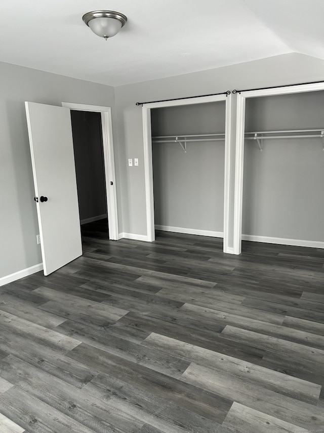 unfurnished bedroom with vaulted ceiling, baseboards, dark wood-style flooring, and two closets