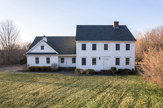 view of front of property with a front lawn, roof with shingles, and a chimney