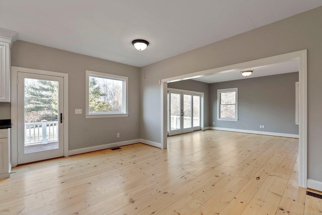 unfurnished dining area with visible vents, light wood-style flooring, french doors, and baseboards