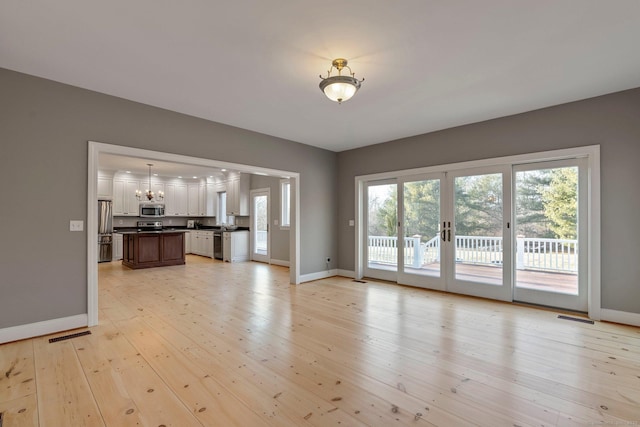 unfurnished living room with light wood-style flooring, a notable chandelier, baseboards, and visible vents