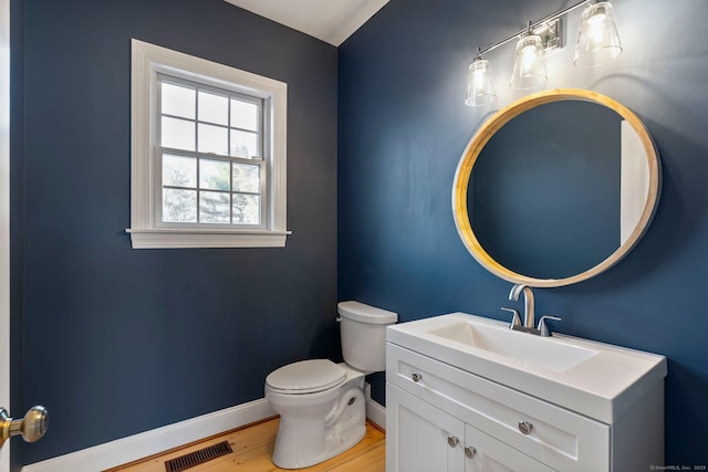 half bathroom with vanity, wood finished floors, baseboards, visible vents, and toilet