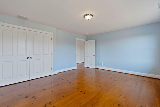 unfurnished bedroom with a closet, visible vents, baseboards, and hardwood / wood-style flooring