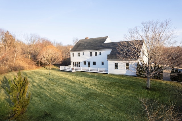 rear view of property with a lawn, roof with shingles, a deck, and a chimney