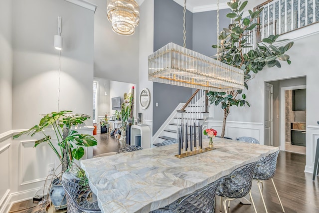 dining space featuring dark wood-style floors, a notable chandelier, a decorative wall, stairway, and a high ceiling