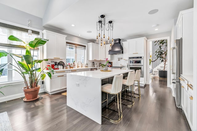 kitchen with stainless steel appliances, premium range hood, a kitchen island, white cabinetry, and hanging light fixtures