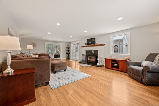 living room with a brick fireplace, a healthy amount of sunlight, and light wood-type flooring