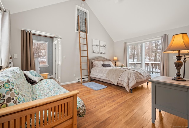 bedroom with a baseboard heating unit, light hardwood / wood-style flooring, and high vaulted ceiling