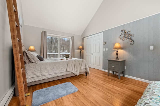 bedroom featuring hardwood / wood-style flooring, a baseboard radiator, high vaulted ceiling, and a closet