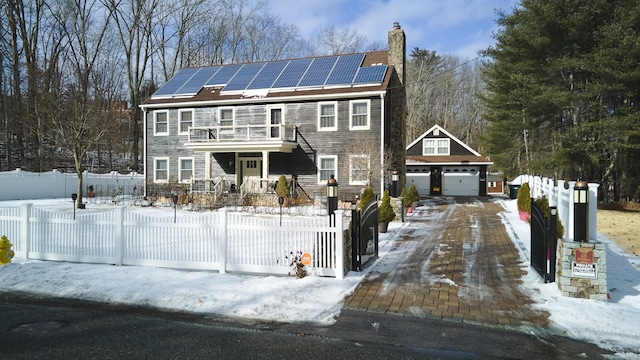 colonial home with a fenced front yard, a chimney, solar panels, driveway, and an outdoor structure