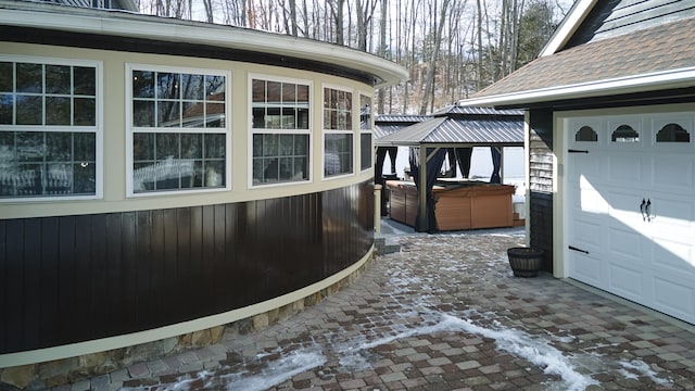 snow covered property with a garage, a gazebo, a shingled roof, and a hot tub