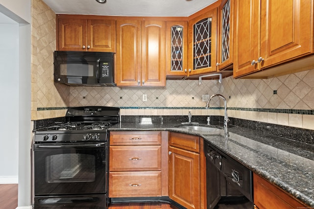 kitchen featuring dark stone counters, black appliances, a sink, and brown cabinets