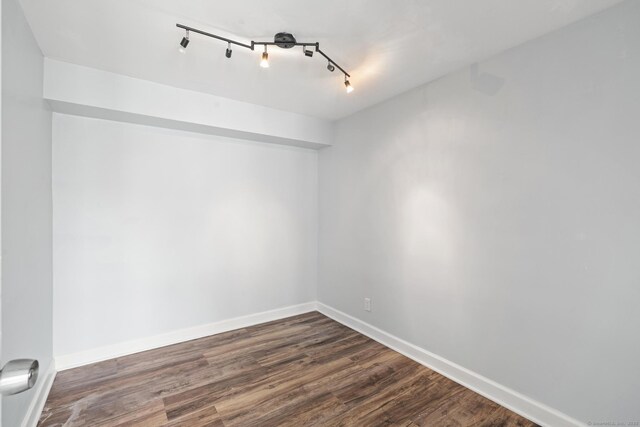 spare room with rail lighting, dark wood finished floors, and baseboards