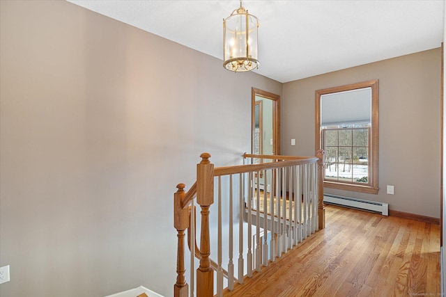 hall featuring an inviting chandelier, light wood-type flooring, and a baseboard heating unit