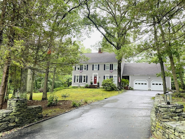 colonial inspired home featuring driveway, a garage, a chimney, and a front yard