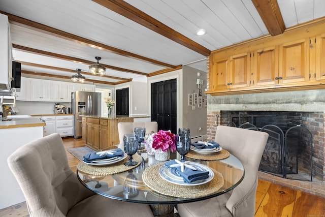 dining area featuring ornamental molding, light wood finished floors, beamed ceiling, and a brick fireplace