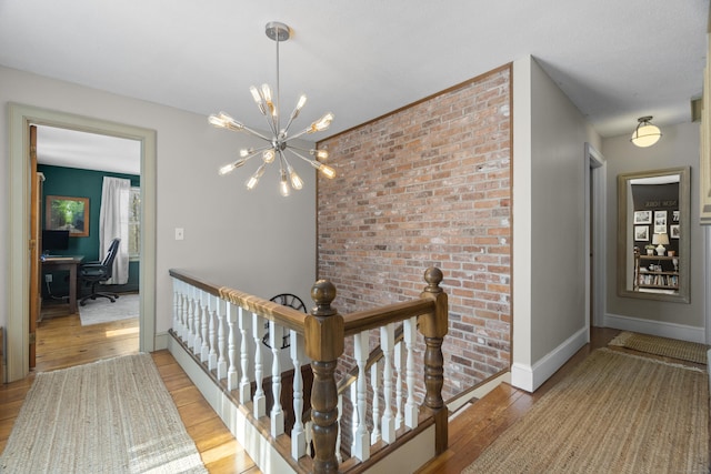 hall featuring light wood-type flooring, baseboards, a chandelier, and an upstairs landing