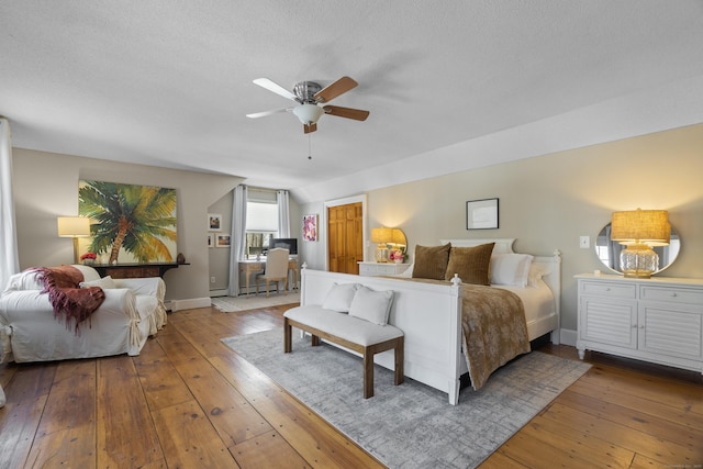 bedroom with a ceiling fan, a textured ceiling, baseboards, and wood finished floors