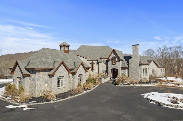 french provincial home with aphalt driveway, stone siding, and a chimney