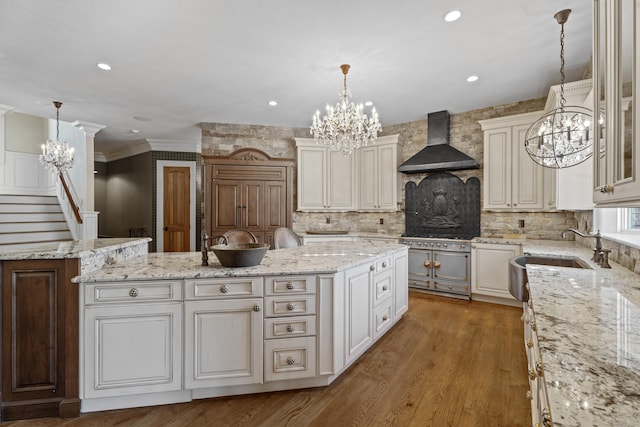 kitchen with decorative light fixtures, a sink, a kitchen island, wall chimney range hood, and glass insert cabinets