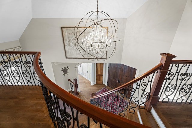 stairs with lofted ceiling, a notable chandelier, and wood finished floors