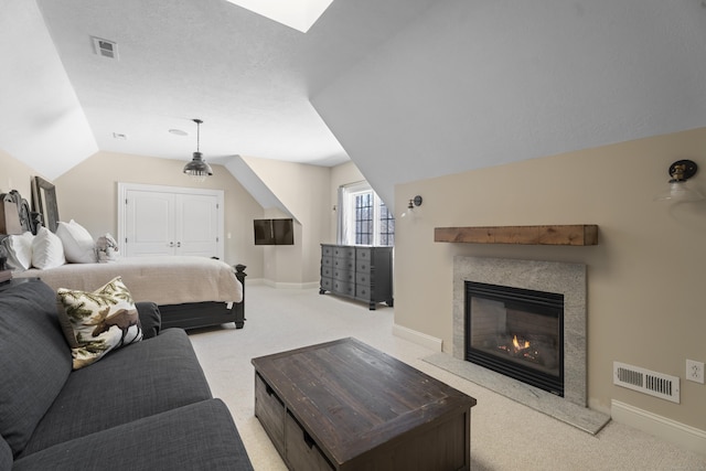 bedroom featuring lofted ceiling, a glass covered fireplace, visible vents, and light colored carpet