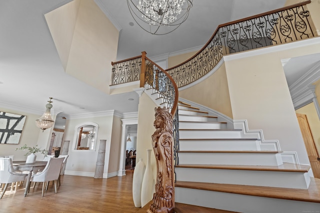 staircase with a towering ceiling, an inviting chandelier, crown molding, and wood finished floors