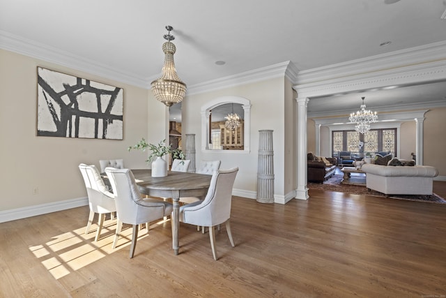 dining area featuring a chandelier, crown molding, decorative columns, and wood finished floors