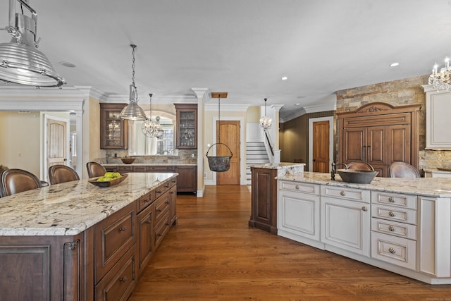 kitchen with dark wood-style floors, glass insert cabinets, a breakfast bar, decorative light fixtures, and a large island with sink