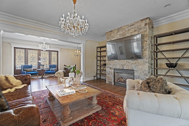 living room featuring ornamental molding, a stone fireplace, an inviting chandelier, and wood finished floors