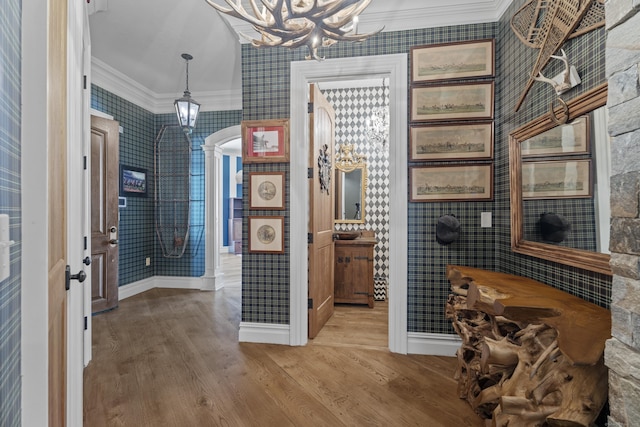 interior space featuring a notable chandelier, wallpapered walls, wood finished floors, and crown molding