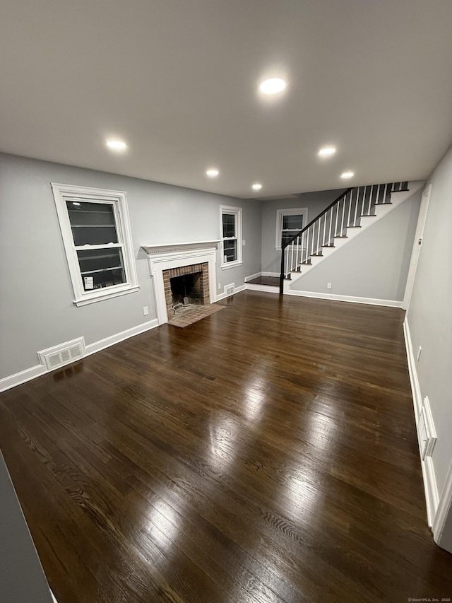 unfurnished living room with stairs, dark wood-type flooring, visible vents, and baseboards