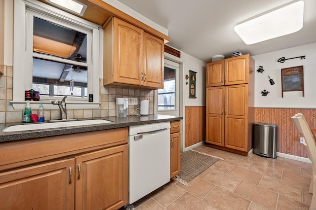 kitchen with wooden walls, dishwasher, dark countertops, a wainscoted wall, and a sink