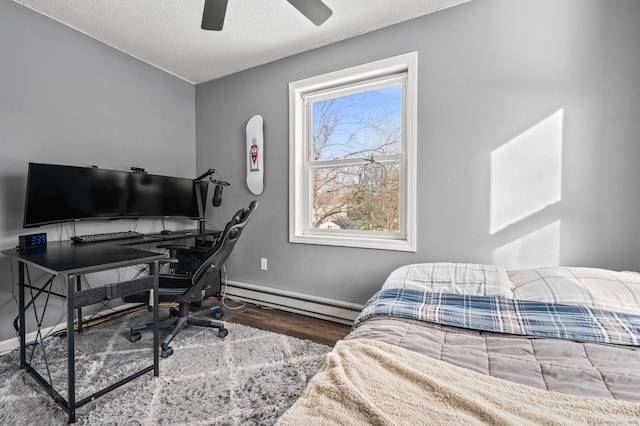 bedroom featuring a textured ceiling, a baseboard heating unit, wood finished floors, a ceiling fan, and baseboards