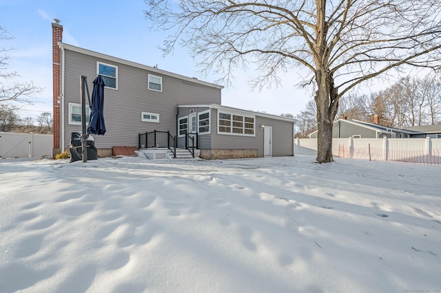 snow covered house with a chimney and fence