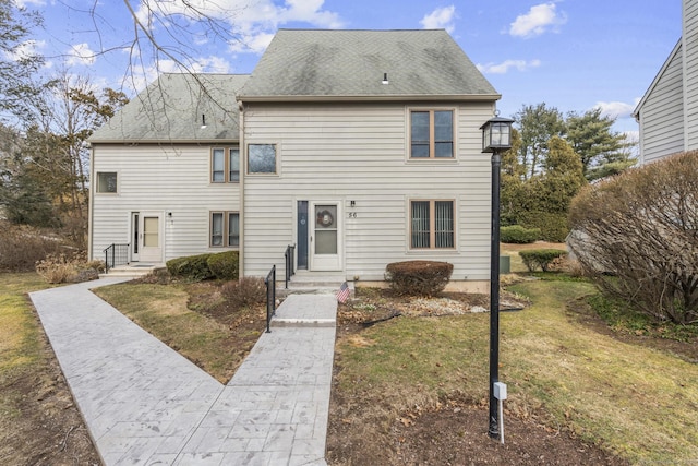 view of front of property featuring entry steps, a front lawn, and roof with shingles