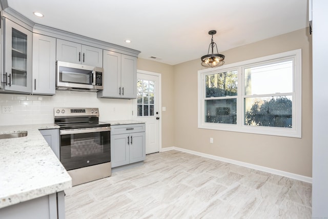 kitchen with gray cabinetry, light stone counters, appliances with stainless steel finishes, pendant lighting, and decorative backsplash