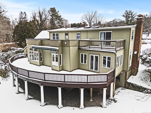 snow covered back of property with a deck and a chimney