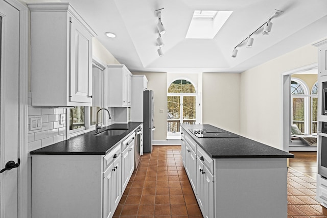 kitchen with appliances with stainless steel finishes, dark countertops, a sink, and white cabinets