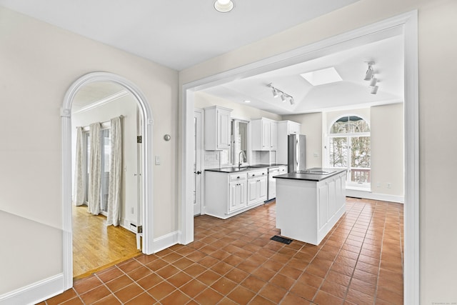 kitchen with a skylight, dark tile patterned flooring, dark countertops, freestanding refrigerator, and white cabinetry