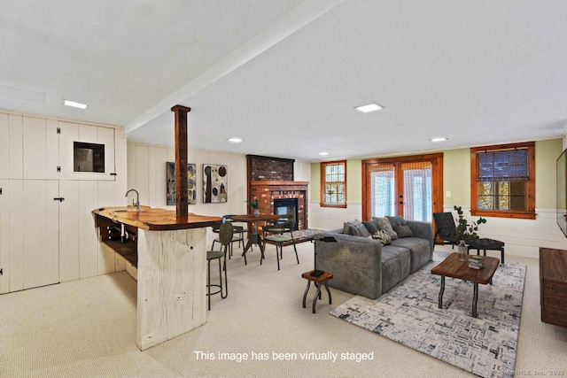 living area with light carpet, a brick fireplace, and wet bar